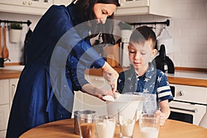 Kid boy helps mother to cook in modern white kitchen. Happy family in cozy weekend morning