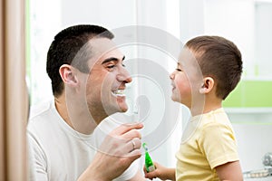 Kid boy and his dad cleaning teeth in bathroom