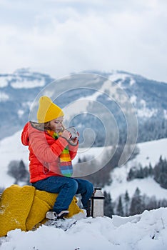 Kid boy hold mug cup with warm tea sit on sleigh ride ouside. Cold winter weather. Warm cup of hot drinks. Cute child