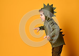 Kid boy in hoodie with dinosaurus spikes at his back and cowl act as a t-rex with his hands claws up and roars