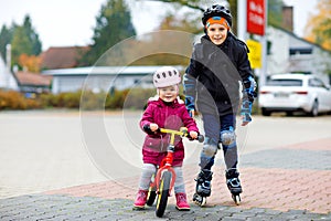 Kid boy and little toddler girl playing together outdoors. Brother in safety clothes skating with rollers. Happy sister