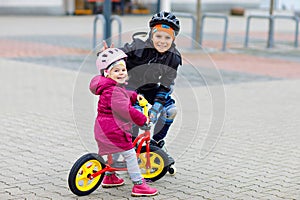 Kid boy and little toddler girl playing together outdoors. Brother in safety clothes skating with rollers. Happy sister