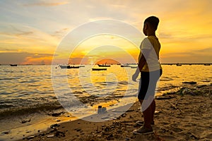 Kid boy looking the sea during sunset with fishing boat background
