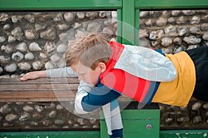 Kid boy is lying on wooden bench in park. Tired child takes an air bath outdoors. Child relaxed after long way walking