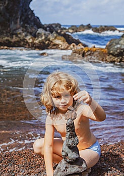 Kid boy making stack of pebbles stone against sea background for spa, balance, meditation and zen theme.