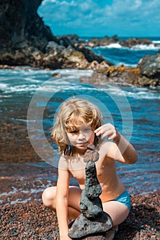 Kid boy making stack of pebbles stone against sea background for spa, balance, meditation and zen theme.