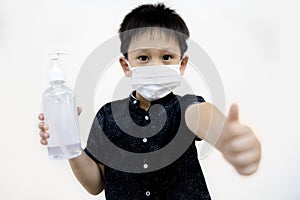 Kid boy in a mask thumbs up,hold a bottle of alcohol antiseptic gel for disinfection,equipment for cleaning hands during pandemic