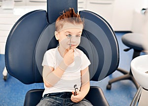 Kid boy in modern dental chair plays with a dental mirror and smiles