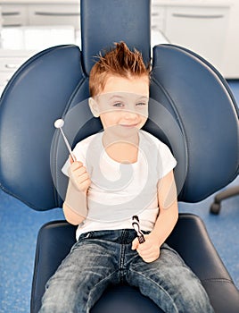 Kid boy in modern dental chair shows us a dental mirror and winks