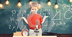 Kid boy near microscope, clock in classroom, chalkboard on background. First former confused with studying, learning