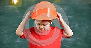 Kid boy in orange hard hat or helmet, chalkboard on background. Child dreaming about future career in architecture or