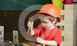 Kid boy in orange hard hat or helmet, study room background. Boy play as builder or repairer, work with tools. Childhood