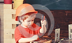 Kid boy in orange hard hat or helmet, study room background. Boy play as builder or repairer, work with tools. Childhood