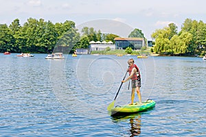 Kid boy paddling on sup board on a lake. Active child on modern trendy stand up paddle board. Summer outdoors vacations