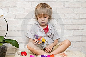 Kid boy playing with building blocks at home or kindergarten with bare feet on warm sheep`s clothing