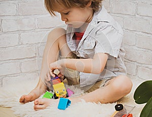 Kid boy playing with building blocks at home or kindergarten with bare feet on warm sheep`s clothing