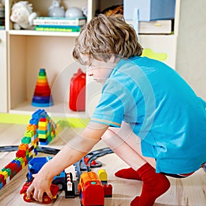 Kid boy playing with colorful plastic blocks and creating train station. Child having fun with building railway toys