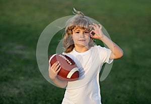 Kid boy playing with rugby ball in park. Kid boy having fun and playing american football on green grass park.
