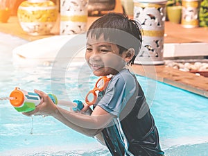 Kid boy is playing with splash water gun on a swimming pool in Thailand tropical resort