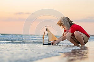 Kid boy playing with toy boat in sea water. Happy holiday by the sea. Kid dreaming about sailing. Happy kid playing with