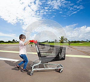 Kid boy pushing empty shopping cart at parking lot