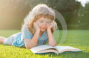 Kid boy reading a book lying on grass. Cute little child in casual clothes reading a book and smiling while lying on