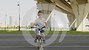 Kid boy is riding a bike on road with cityscape background in slow motion.