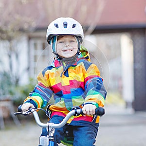 Kid boy in safety helmet and colorful raincoat riding bike, outd