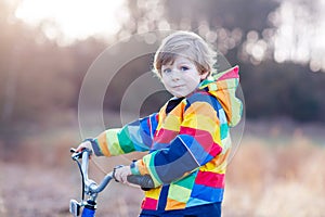 Kid boy in safety helmet and colorful raincoat riding bike, outd