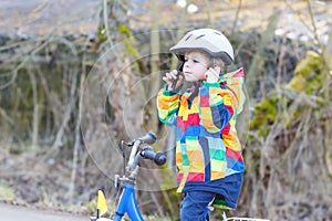 Kid boy in safety helmet and colorful raincoat riding bike, outd