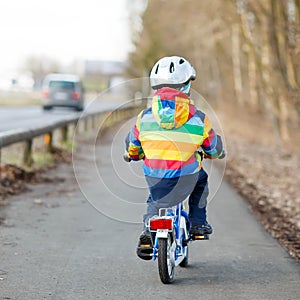 Kid boy in safety helmet and colorful raincoat riding bike, outd