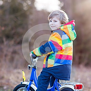 Kid boy in safety helmet and colorful raincoat riding bike, outd