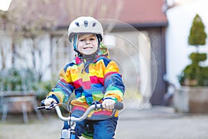 Kid boy in safety helmet and colorful raincoat riding bike, outd