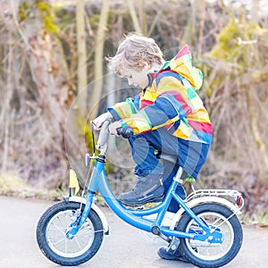 kid boy in safety helmet and colorful raincoat riding bike, outd