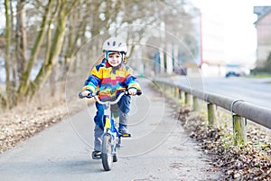 Kid boy in safety helmet and colorful raincoat riding bike, outd