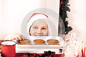Kid boy in Santa cap taking try to steal cookie from table.