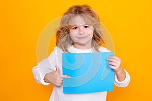 Kid boy with sheet of paper, isolated on yellow background. Portrait of a kid holding a blank placard, poster. Empty