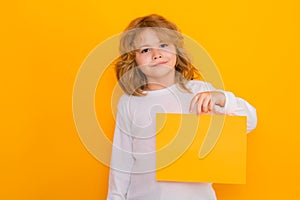 Kid boy with sheet of paper on yellow background. Child holding a blank placard, poster. Empty board for templates