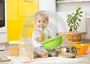 Kid boy sitting on the kitchen floor and playing with flour.