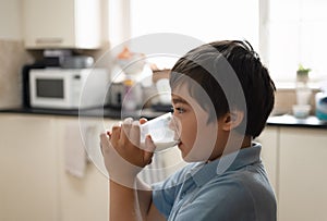 Kid boy standing in kitchen drinking grass of warm milk for breakfast before go to school. Healhty food liftstyle for children