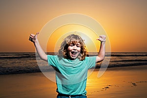 Kid boy on sunset beach, raised hands. Amazed surprised kids emotions.