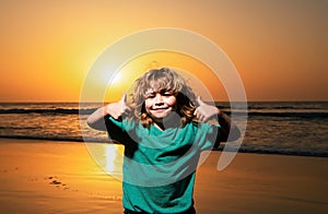 Kid boy on sunset beach, thumbs up. Amazed surprised kids emotions.