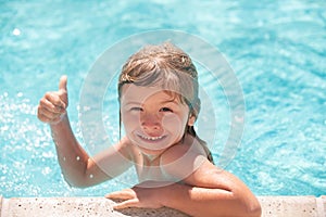 Kid boy swim in swimming pool with thumbs up. Happy little kid boy playing with in outdoor swimming pool on hot summer