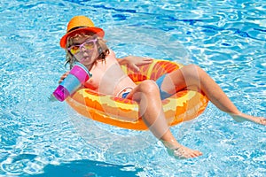 Kid boy in swimming pool on inflatable ring. Children swim with orange float. Water toy, healthy outdoor sport activity