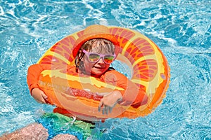 Kid boy in swimming pool on inflatable ring. Children swim with orange float. Water toy, healthy outdoor sport activity