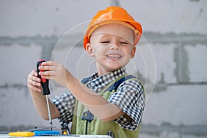 Kid boy twists bolt with screwdriver. Child repairman with repair tool. Child in helmet and boilersuit on construction