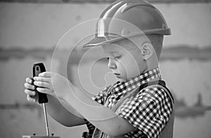 Kid boy twists bolt with screwdriver. Child repairman with repair tool. Child in helmet and boilersuit on construction