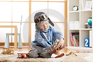 Kid boy weared aviator helmet plays with wooden toy planes in his children room