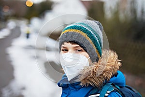Kid boy wearing ffp medical mask on the way to school. Child backpack satchel. Schoolkid on cold autumn or winter day