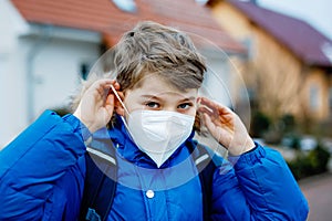 Kid boy wearing ffp medical mask on the way to school. Child backpack satchel. Schoolkid on cold autumn or winter day